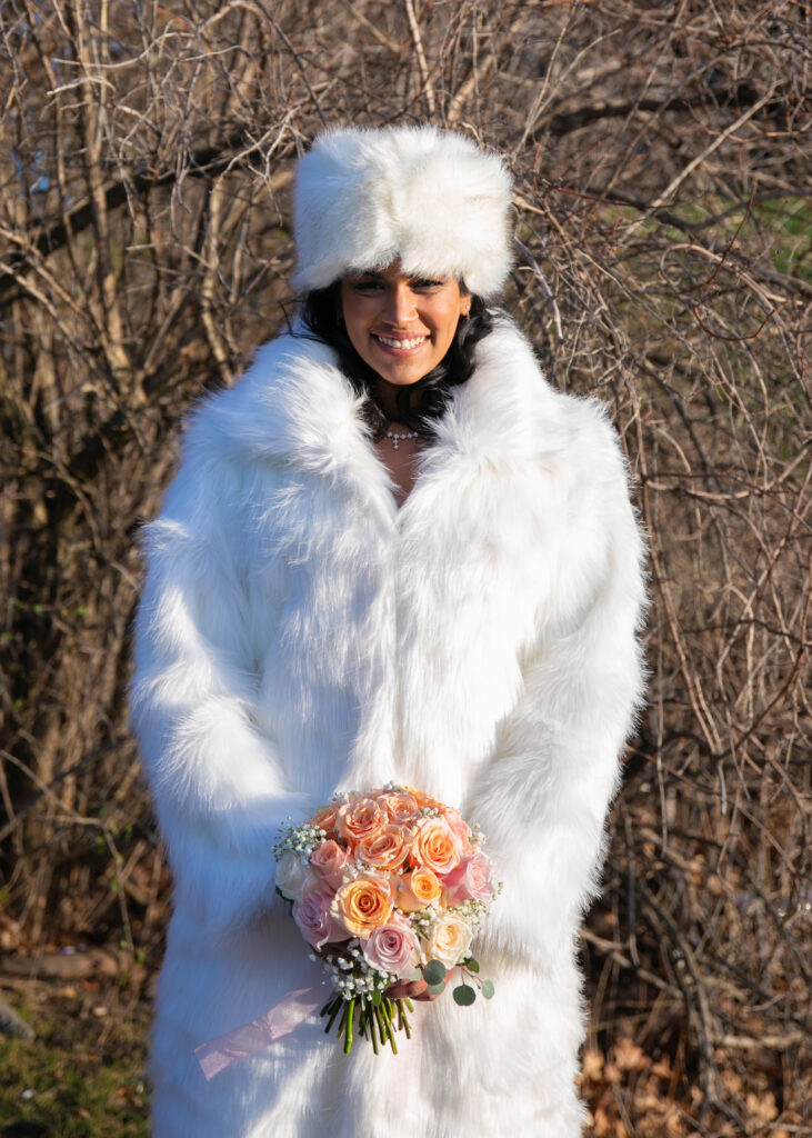 Indian Bride wearing beautiful white fur winter jacket holding flowers.